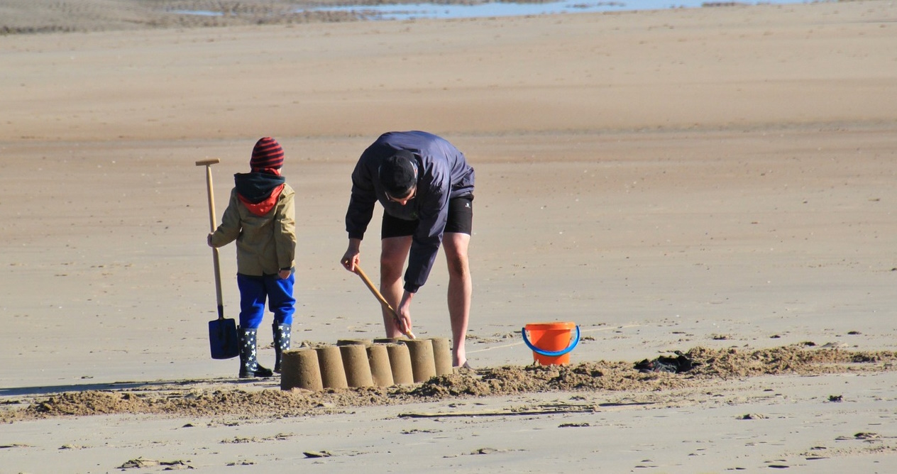 Un hombre hace un castillo de arena en la playa junto a un niño