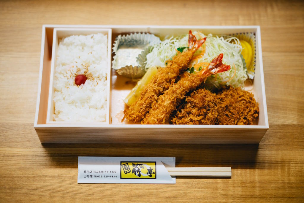 El bentō es una forma de comida para llevar muy popular en Japón que ha encontrado su lugar en los restaurantes japoneses en España. Consiste en una caja que divide la comida en pequeñas porciones, incluyendo arroz, pescado o carne, y uno o varios acompañamientos como verduras encurtidas o fruta. Lo que lo hace especialmente atractivo es su presentación, donde cada elemento está cuidadosamente colocado para disfrutar tanto con los ojos como con el paladar. Un aspecto curioso es que en Japón, preparar un bentō puede ser considerado un acto de amor, ya que madres y esposas suelen dedicar tiempo y esfuerzo en prepararlos para sus hijos y esposos, respectivamente, como muestra de cuidado y atención.