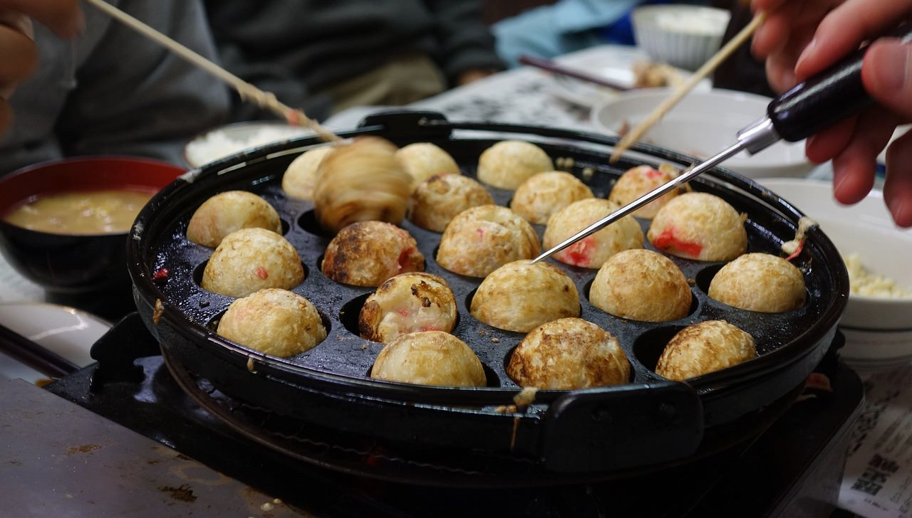 Bolas de masa a base de harina cocinadas en una plancha especial y rellenas de trozos de pulpo, cebollín, jengibre encurtido y tempura. Se sirven con salsa takoyaki, mayonesa, aonori (algas marinas en polvo) y katsuobushi (virutas de bonito seco). En España, el takoyaki es apreciado en festivales y restaurantes japoneses como un bocado delicioso y divertido, ofreciendo una experiencia culinaria única y un sabor que captura la esencia de la comida callejera japonesa.