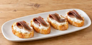 Pintxo de anchoa y crema de queso Filetes de anchoa plegados sobre queso crema blanco y rebanadas de pan.