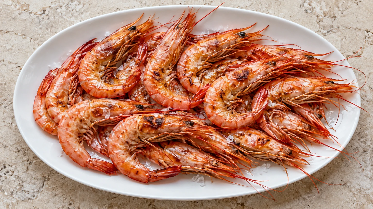 Gambas enteras a la plancha con cristales de sal sobre una fuente blanca.