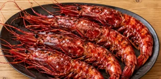 Carabineros a la plancha Carabineros enteros de color rojo intenso a la plancha sobre una fuente oscura.