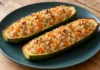Calabacines rellenos de quinoa Dos mitades de calabacín rellenas de quinoa, zanahoria y nueces sobre un plato azul verdoso.