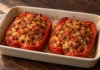 Pimientos rellenos de arroz y lentejas Dos mitades de pimiento rojo asado rellenas de arroz, lentejas y tomate en una fuente de cerámica.