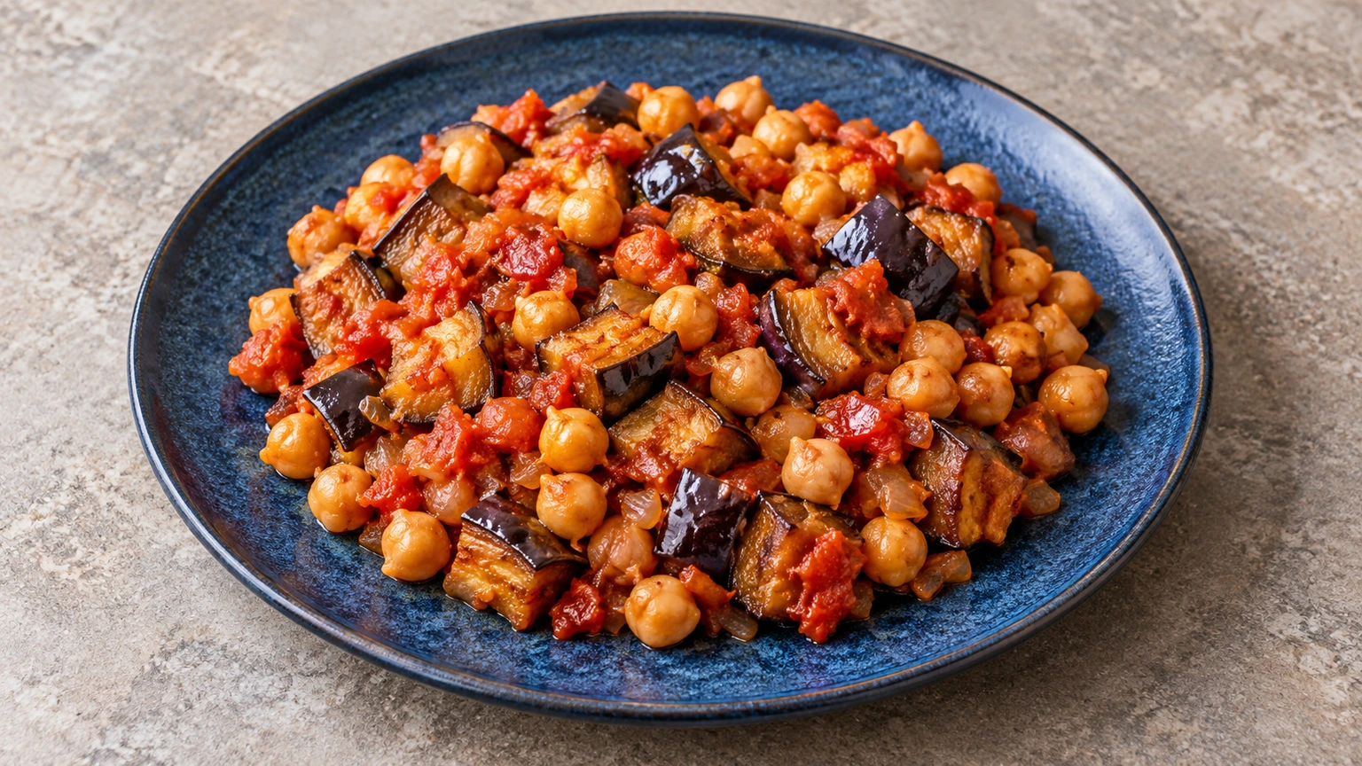 Garbanzos salteados con dados de berenjena de piel morada y tomate en un plato azul.