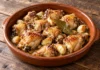 Trozos de pollo dorado con dientes de ajo y laurel en una cazuela de barro.