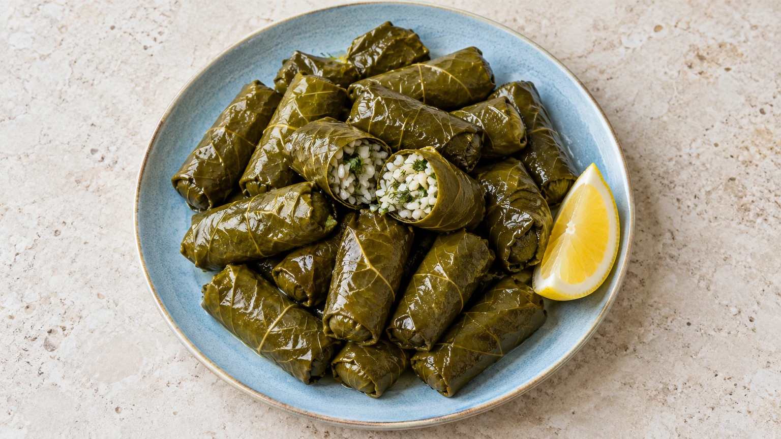 Rollitos de hojas de parra con uno abierto que muestra arroz y hierbas, acompañados de limón.