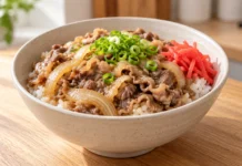 Cuenco de gyudon con arroz blanco, ternera en lonchas finas, cebolla, cebolleta y jengibre encurtido rojo.
